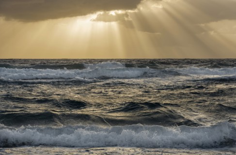 Sun rays streaking from clouds over ocean waves