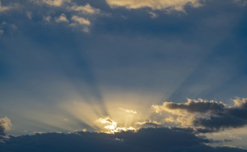 Sun rays streaking upwards from clouds against sky