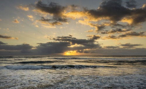 Ocean and dramatic golden streaks from morning clouds