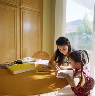 Two girls (10-11) doing homework at kitchen table