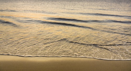 Close-up of calm ocean surf washing up onto beach at sunrise