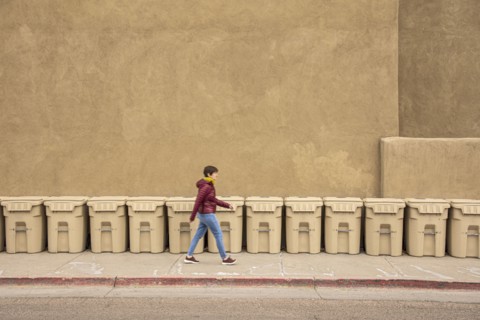 USA, New Mexico, Santa Fe, Woman walking past row of garbage bins