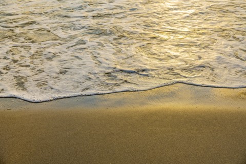 Close-up of calm ocean surf washing up onto beach at sunset
