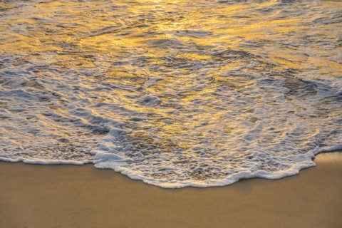 Close-up of calm ocean surf washing up onto beach at sunset