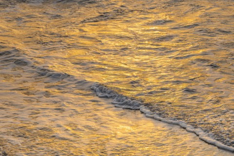 Close-up of calm ocean surf washing up onto beach at sunset