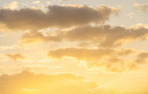 Cumulus clouds against pale golden sky at sunrise
