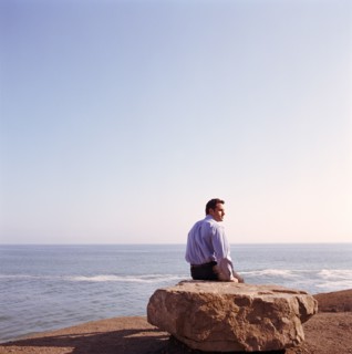 USA, California, Point Mugu, Businessman sitting on rock on beach