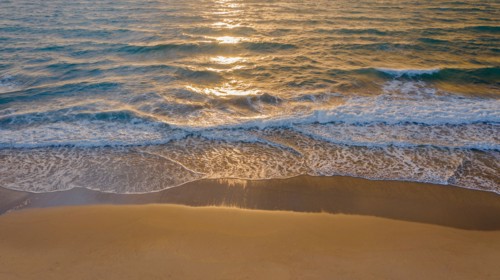 Calm ocean waves rolling onto sandy beach at sunrise