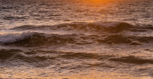 Close-up of ocean waves washing beach at sunrise