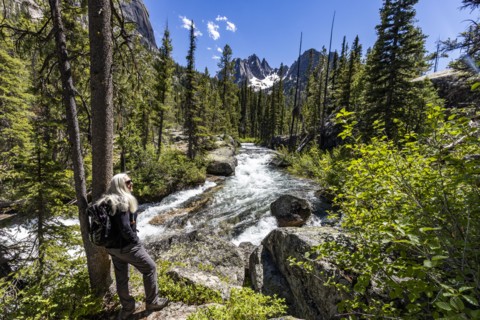 Senior blonde woman hiking by rushing stream in mountains near Sun Valley