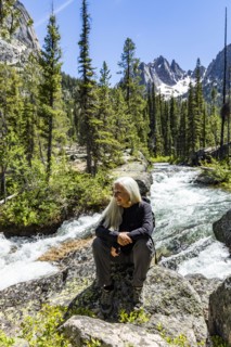 Senior blonde woman hiking by rushing stream in mountains near Sun Valley