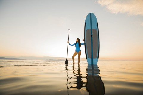 Portrait of woman in blue swimsuit standing with paddleboard in lake at sunset