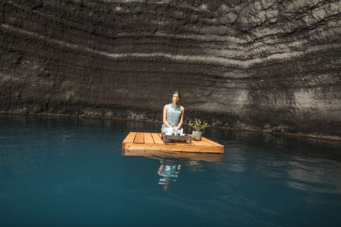Beautiful woman kneeling on wooden raft on pond