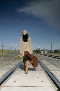 Woman with guitar walking down railroad tracks