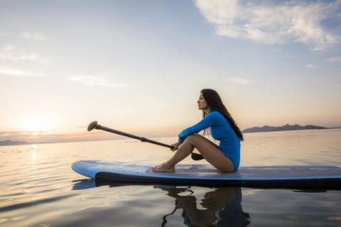 Woman sitting on paddleboard at sunset