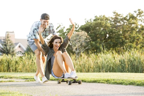 Man pushing woman sitting on longboard in park
