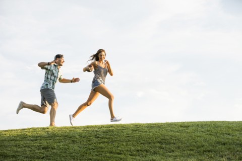Woman and man running on grassy hill in park