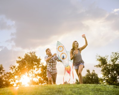 Woman and man running with kite in park at sunset