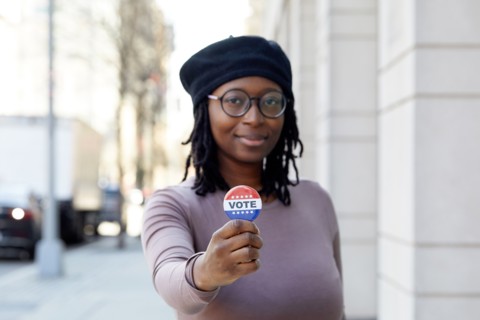 Portrait of smiling woman showing Vote button in city