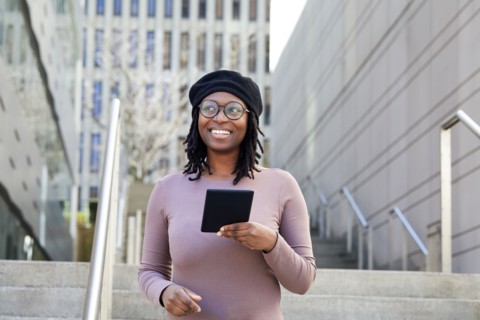Smiling woman wearing eyeglasses and beret holding digital tablet in city