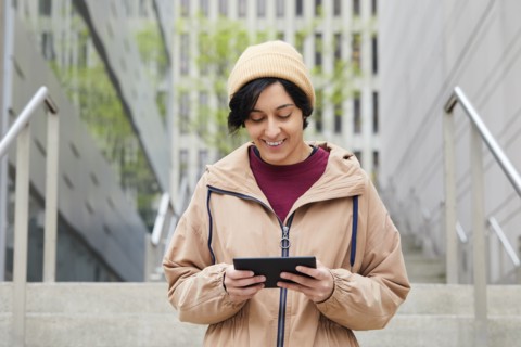 Smiling woman holding digital tablet on steps in city