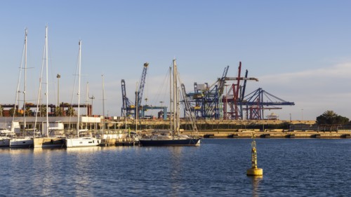 Sailboats moored at marina with dock cranes in background