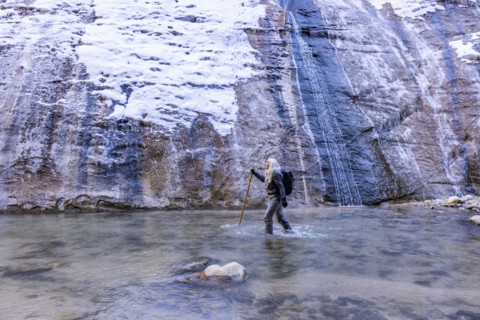 Senior woman crossing river while hiking in mountains