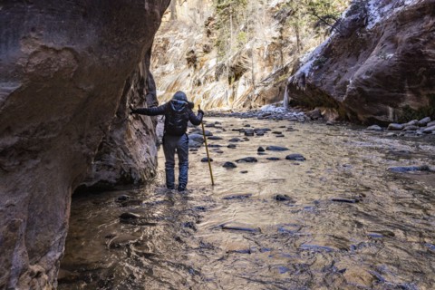 Senior woman crossing river while hiking in mountains