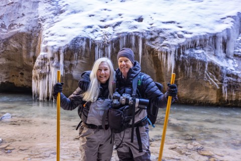 Senior couple crossing river while hiking in mountains