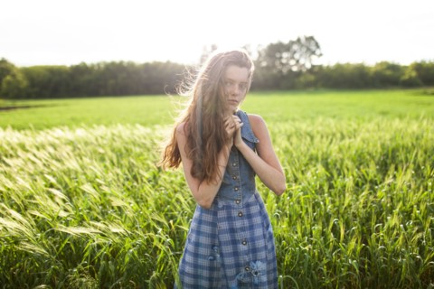 Portrait of woman standing with hands clasped in field