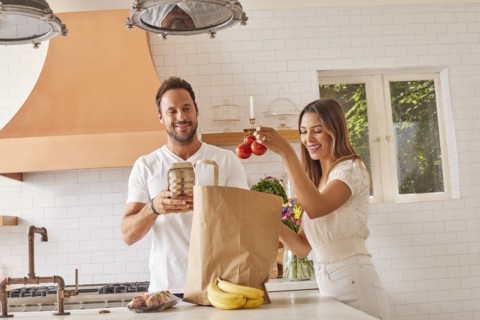 Smiling couple with paper shopping bag and groceries in kitchen