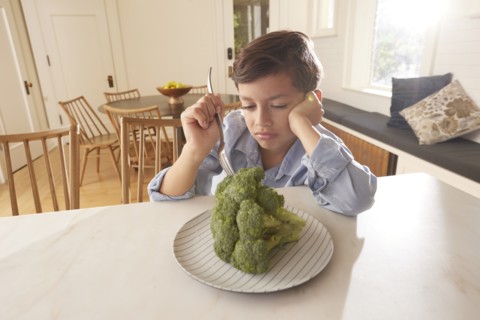 Displeased boy looking at broccoli on plate