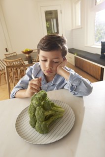 Displeased boy looking at broccoli on plate