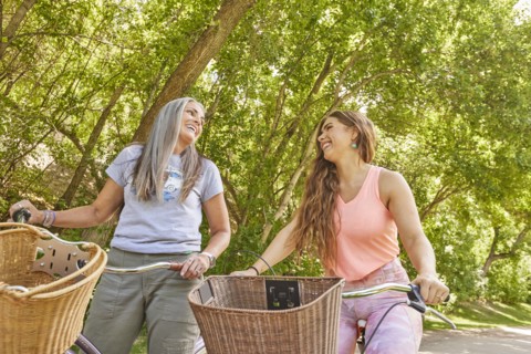 Mother and adult daughter riding bicycles in park