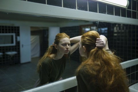 Young woman looking in mirror in public bathroom