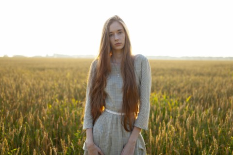 Portrait of young woman looking at camera while standing in field