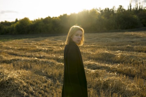 Portrait of young woman standing in field at sunset