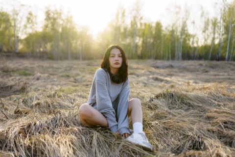 Brunette woman wearing grey sweatshirt sitting in meadow