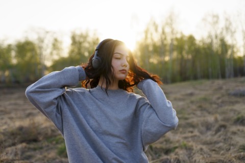 Portrait of woman listening to music with closed eyes in meadow at sunset