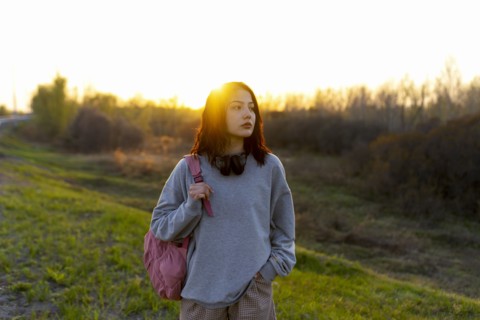 Woman wearing grey sweatshirt standing in meadow at sunset