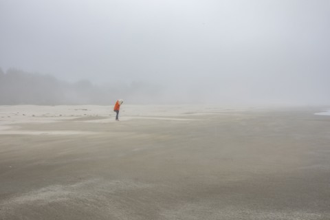 Woman in orange jacket standing on foggy beach