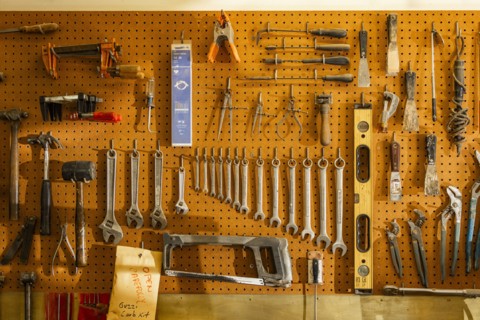 Tools on pegboard hooks on wall of wood and metal shop