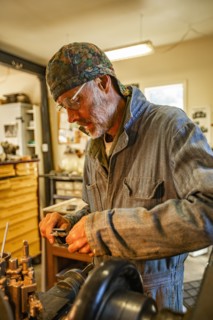 Senior artisan wood and metal craftsman works with tools in workshop
