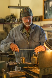 Senior artisan wood and metal craftsman works with tools in workshop