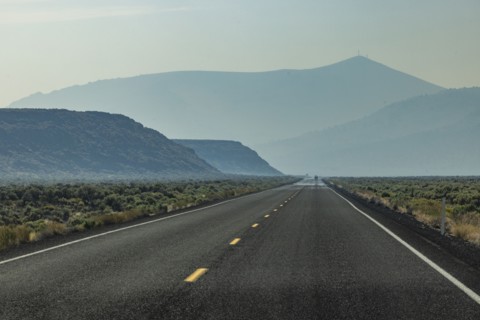 Empty highway leading through desert with mountains in background