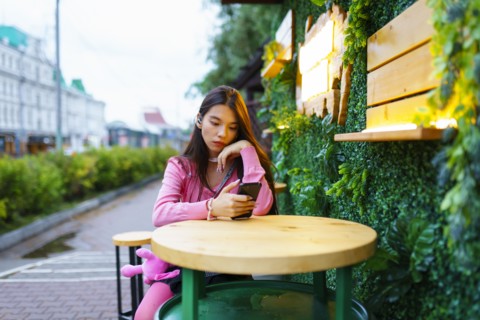 Young woman with smartphone sitting in sidewalk cafe