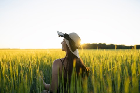 Rear view of woman in straw hat standing in field at sunset