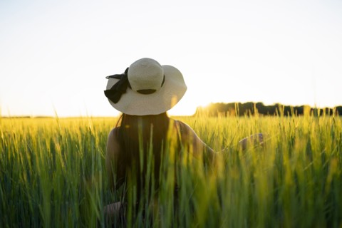 Rear view of woman in straw hat standing in field at sunset