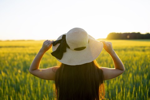 Rear view of woman in straw hat standing in field at sunset
