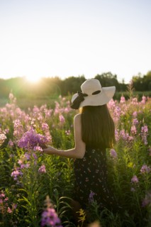 Rear view of woman in straw hat standing in meadow at sunset